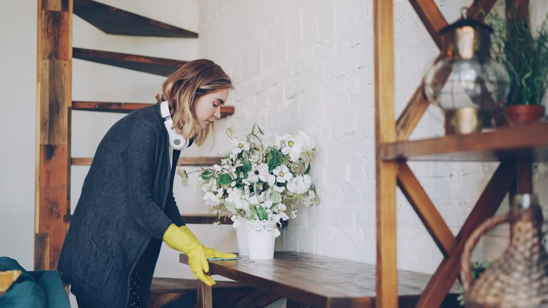 Two women in work clothes cleaning a modern living room using a vacuum and mop.