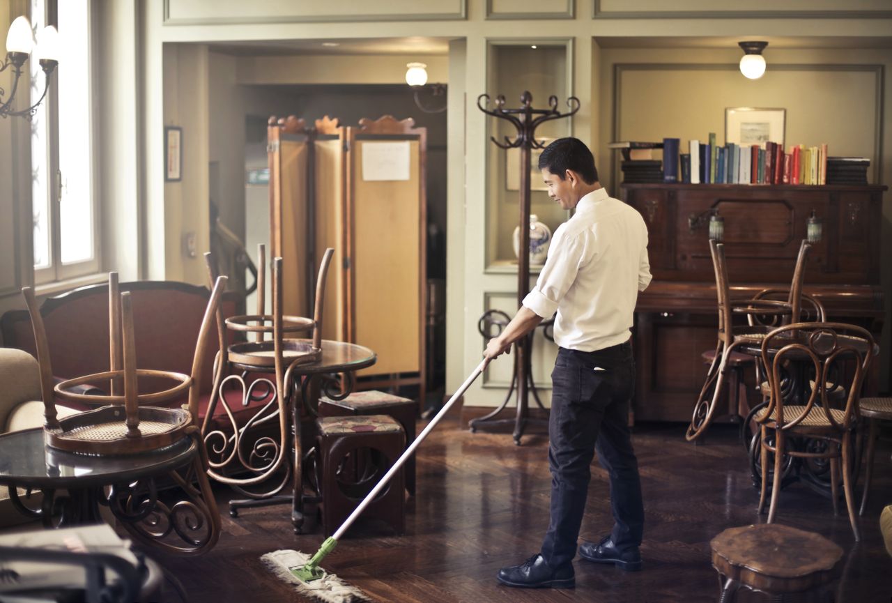 services-03 Side view of young ethnic male in uniform cleaning floor with mop while working in retro styled restaurant
